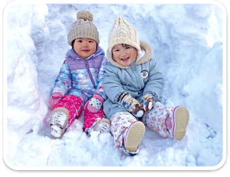 雪の中で楽しそうに並んで座る園児たち